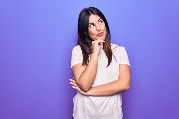 Sticker - Young beautiful brunette woman wearing casual t-shirt standing over purple background thinking concentrated about doubt with finger on chin and looking up wondering