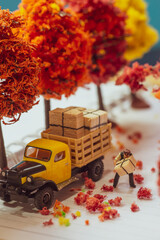 Top view miniature toy figurines of alone courier man holding delivery box  in autumn, fall season or during cherry blossom season concept -  warm tone filter applied.