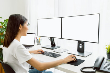 Wall Mural - Young Asian woman sitting on chair and working at the computer with blank screen in home on the day light shone in the afternoon.