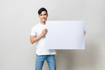 Portrait of handsome Asian man holding empty white placard in isolated studio gray background