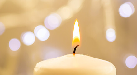 Close up of one burning candle with blurred Christmas light background