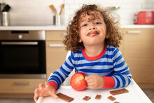 Smiling Toddler With Curly Hair And Chocolate Mustache Holding Red Apple