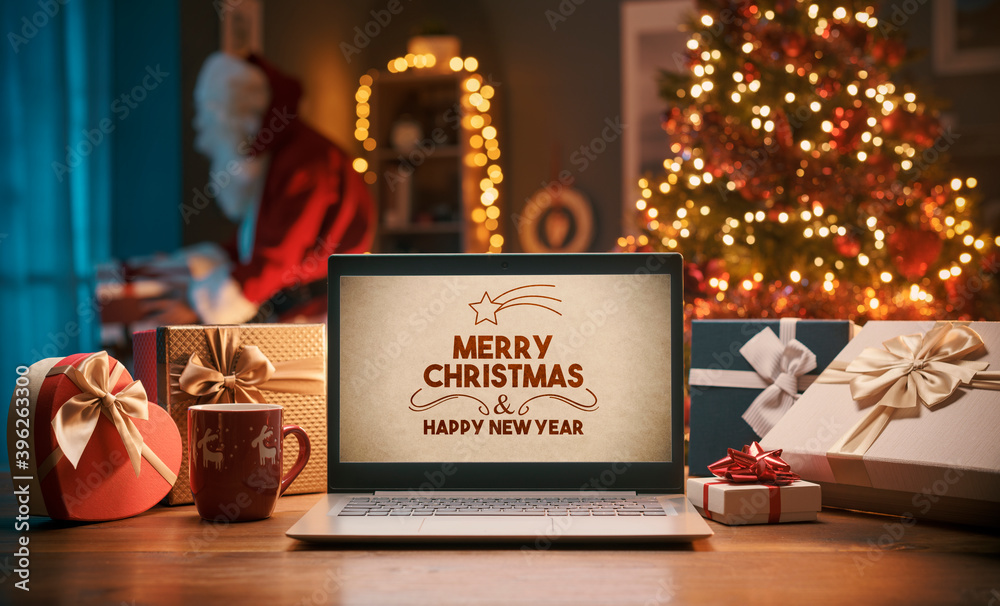 Christmas wishes on a laptop and Santa bringing gifts at home - obrazy, fototapety, plakaty 