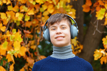 Wall Mural - portrait of a teenager listening to music by headphones, relaxing in autumn city park, bright yellow maple leaves as background