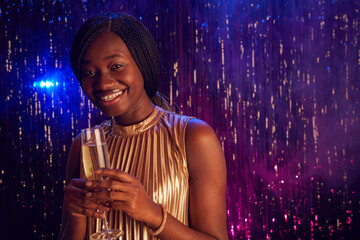 Portrait of teenage African-American girl holding champagne glass and smiling at camera while enjoying party at prom night, copy space