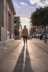 black afro american man with yellow sweatshirt turned back walking down city street with sun in background