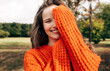 © iuricazac - A gorgeous young woman enjoys the weather, wearing an orange knitted sweater posing on a nature background. The pretty female has a dreamy expression, resting outdoors in the park.
