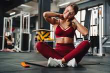 Unhappy Athletic Sportswoman With Neck Pain Sitting On Mat In Gym