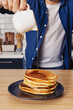 Man pouring with maple syrup on the stack of pancakes