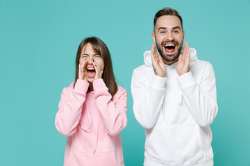 Canvas Print - Cheerful crazy funny young couple two friends man woman 20s wearing white pink casual hoodie screaming with hands gesture near mouth isolated on blue turquoise colour wall background studio portrait.