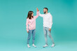 © ViDi Studio - Full length of cheerful young couple two friends man woman in white pink casual hoodie hold hands folded giving high five looking at each other isolated on blue turquoise background studio portrait.