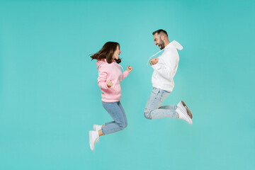 full length side view of joyful young couple friends man woman in white pink casual hoodie jumping d
