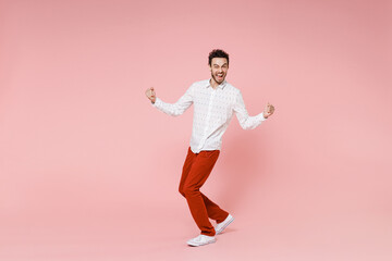 Wall Mural - Full length side view of happy joyful young bearded man 20s wearing basic casual white shirt standing doing winner gesture looking camera isolated on pastel pink color wall background studio portrait.