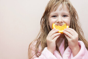 charming blonde girl with wet hair in a pink bath robe eating an orange