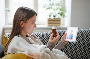 Wall Mural - Young woman having video call with doctor on tablet at home, online consultation concept.