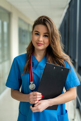 Wall Mural - Doctor in blue medical form with a stethoscope, holding a clipboard standing in hospital