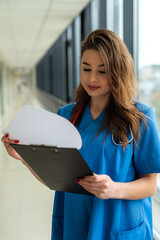 Wall Mural - Doctor in blue medical form with a stethoscope, holding a clipboard standing in hospital