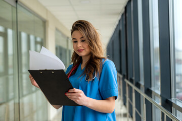 Wall Mural - portrait of beautiful nurse in blue uniform with clipboard in modern hospital