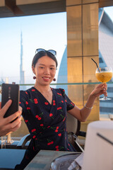 Wall Mural - Woman taking a selfie with a drink with Dubai city view