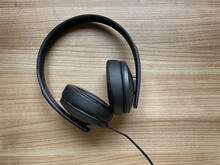Pair Of Black Around-ear Or Over-ear Headphones Lying On Wooden Desk