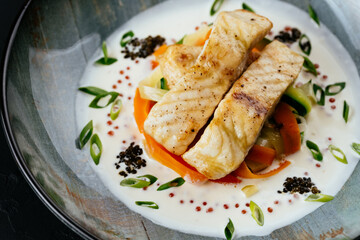 grilled cod fillet with vegetables and sauce on a black backgrou