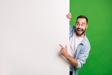 Portrait of optimistic funky guy point empty space wear blue shirt isolated on vibrant green color background