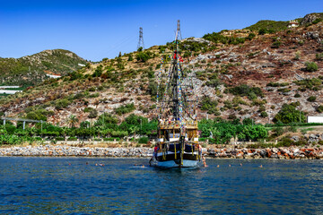 Wall Mural - Vintage pirate tourist boat for a party on the background of a mountain coast - view from the sea. People swim in blue water around a large cruise ship off the coastline of Alanya (Turkey)