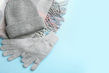 Poster - Stylish gloves, scarf and hat on light blue background, flat lay. Space for text