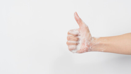 Hand with foam soap bubbles doing a like or thumbs up hand sign on white background.