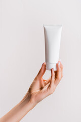 cropped view of woman holding tube of hand cream isolated on grey, stock image