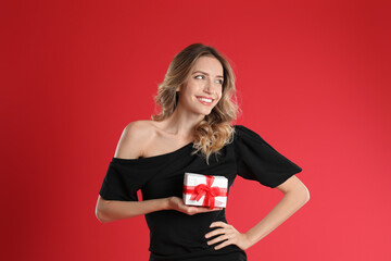 Poster - Beautiful young woman with Christmas present on red background