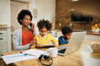 © Drazen - Working black mother with two children talking on cell phone at home.