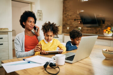 Wall Mural - Working black mother with two children talking on cell phone at home.