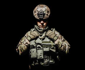 Wall Mural - Photo of a fully equipped shaded soldier in armor vest and helmet standing on black background.