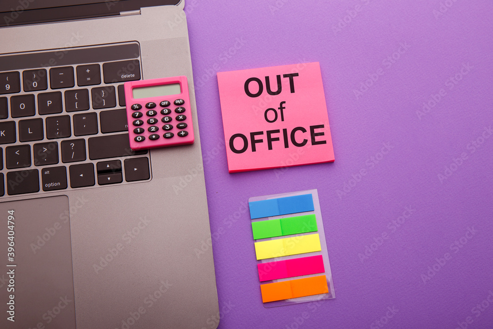 Out of office - message on pink sticky note on work table.