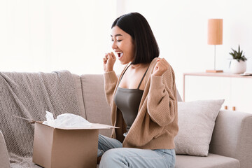 Wall Mural - Overjoyed asian woman unpacking parcel after online shopping