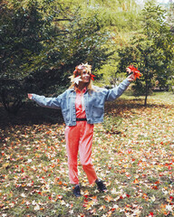 Wall Mural - A girl with a head decorated with red maple leaves and a buget of leaves in her hand stands in a clearing in the park