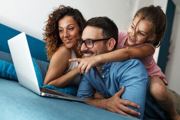 	
Happy family lies on bed and watching something on laptop.Laughing and fun.	
