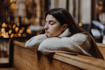 Wall Mural - a young pretty woman came to the temple to pray to God. The parishioner of the church sits on a bench with her hands folded for prayer and heartily prays. copy space