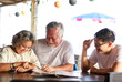 © sutthichai - Happy family.Happy couple of retirement parent enjoy in restuarant with their son for reading a food menu.