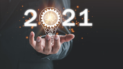Poster - 2021 goal, target business concept, hand of businessman with a light bulb And there is a gear icon . The idea of ​​inspiration from online technology. innovation idea concept.