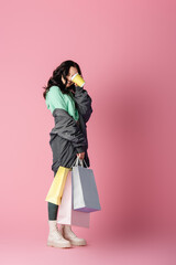 Wall Mural -  brunette young woman in casual winter outfit with shopping bags and coffee to go on pink background