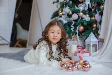 Wall Mural - little Asian girl writes a letter to Santa Claus near the Christmas tree smiles Christmas, new year