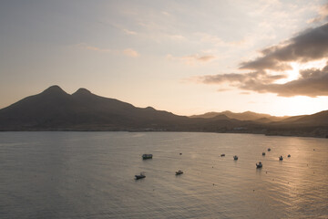 Sunset off the coast with quieter and small fishing boats in the water with the mountains in the background.