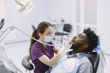 Young african-american man. Guy visiting dentist's office for prevention of the oral cavity. Man and famale doctor while checkup teeth.