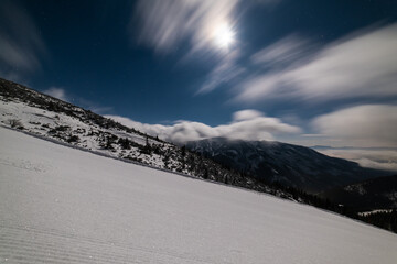 Fresh groomed snow on ski slope at ski resort at cloudy night. Snow groomer tracks on a mountain ski piste.