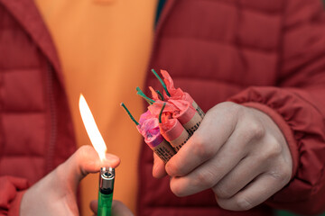 Wall Mural - Man in Red Jacked Lighting Up Several Firecrackers in his Hand Using Gas Lighter. Guy Getting Ready for New Year Fun with Fireworks or Pyrotechnic Products