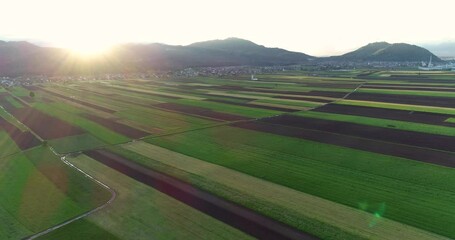 Wall Mural - Aerial drone flying view of grassland meadow agriculture fields in Slovenia at sunset. Railroad between farming fields, hills and small town in the distance. Forward moving