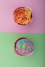 High Angle View Of Two Colourful Cupcakes With Sprinkles On Purple And Green Background