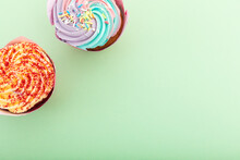 High Angle View Of Two Colourful Cupcakes With Sprinkles On Green Background